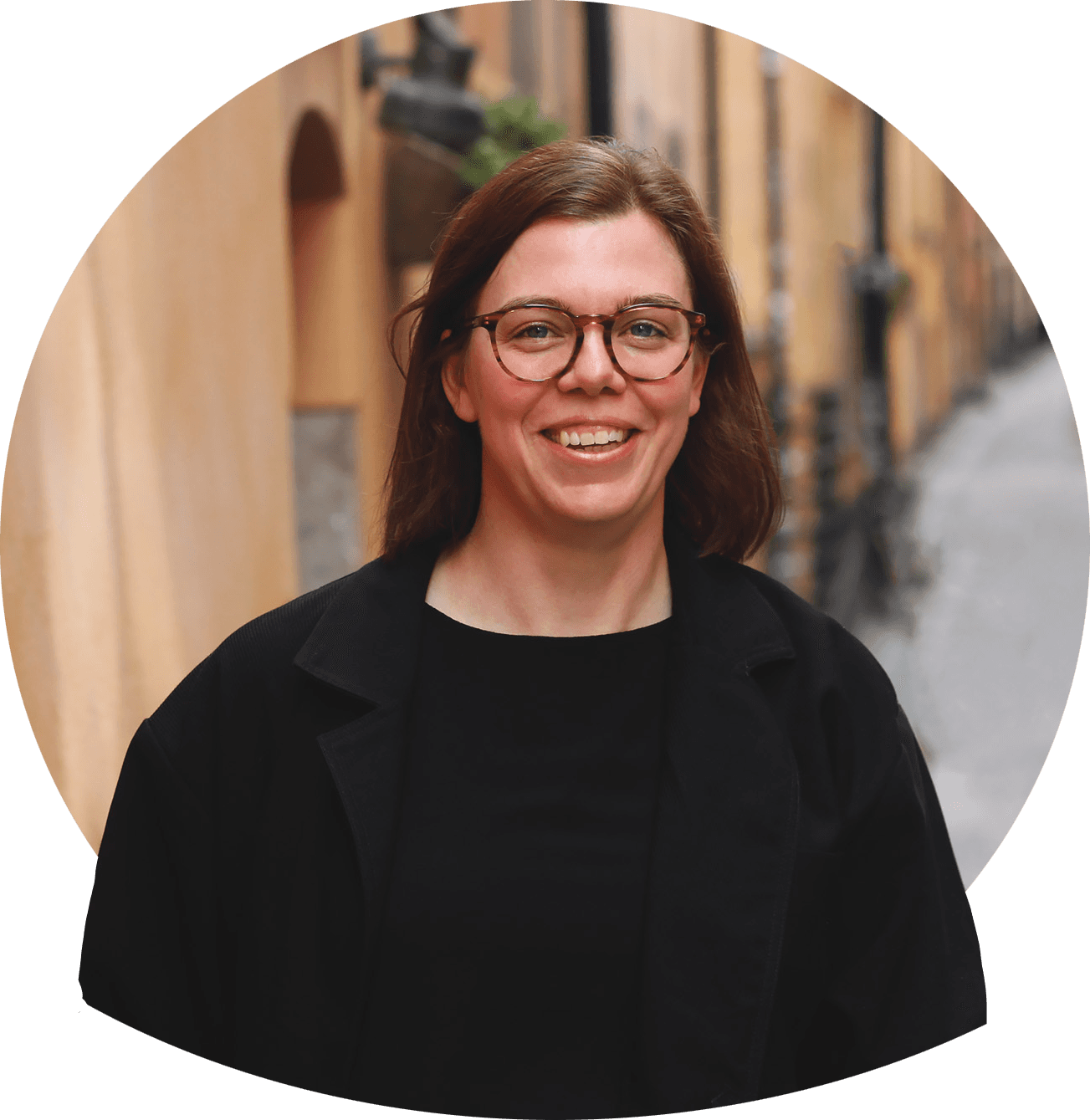 Frida S är glasögonprydd mörkt långt hår i kofta och topp, lutar hakan mot handen. Foto.