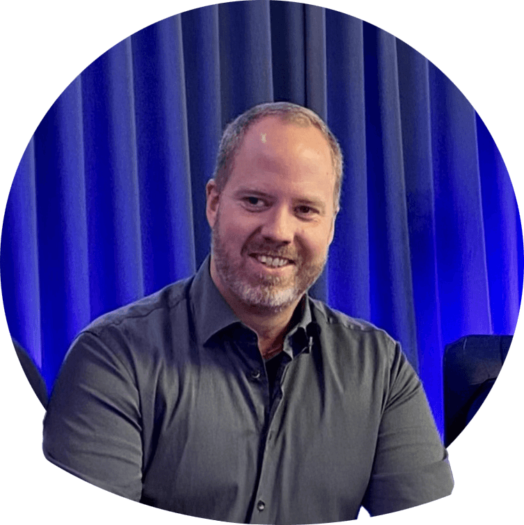 Andreas leende i mörk skjorta, mellanblont hår och kort skägg. Foto.