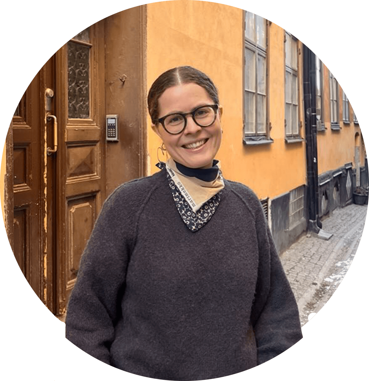 Ingunn, a smiling woman with up-do brown hair and dark glasses. She has a gray knitted sweater and a patterned scarf.