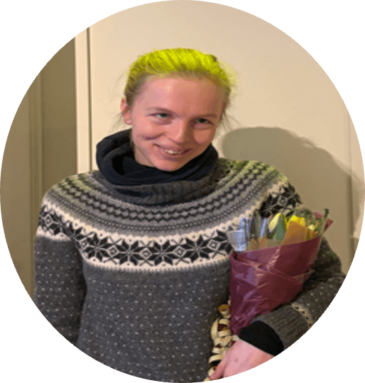 Amalie with light hair, wearing a gray patterned sweater, holding a bouquet of flowers.