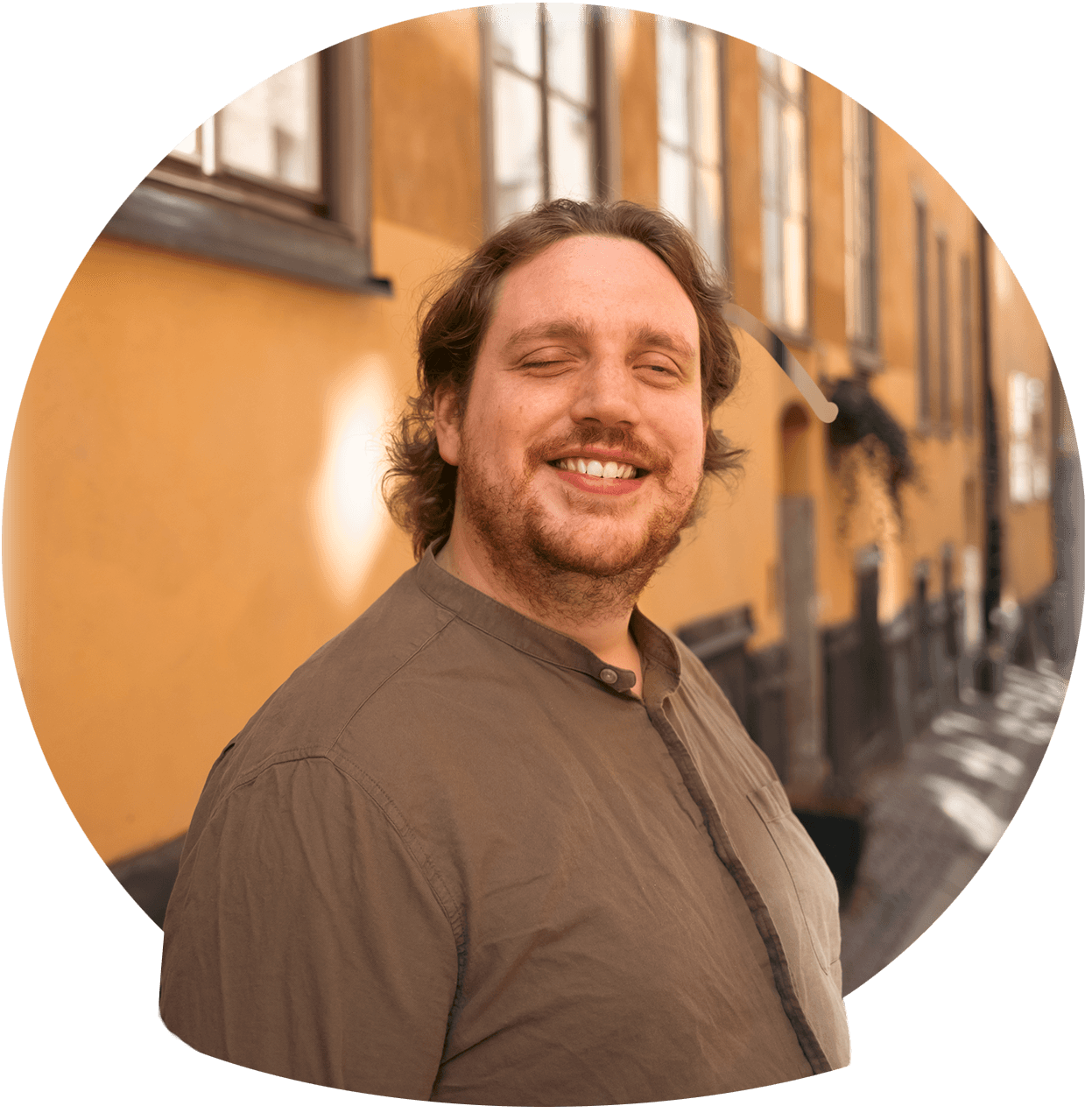 Christoffer en brunhårig man med ett stort leende och lite ansiktsbehåring och en brun skjorta. Foto.