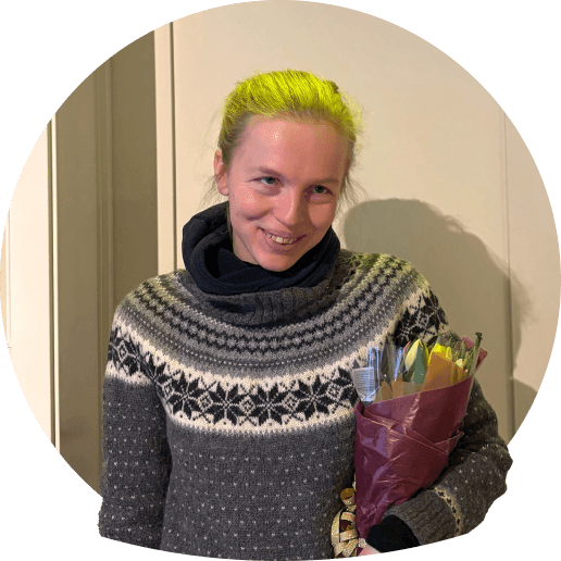 Amalie med ljust hår, klädd i en grå mönstrad tröja, håller en bukett blommor.